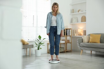 Menopause, weight gain. Concerned woman standing on floor scales at home