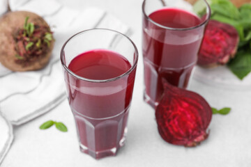 Fresh beet juice in glasses and ripe vegetables on light table, closeup