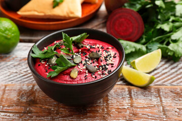 Tasty beetroot hummus in bowl and products on wooden table