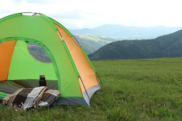 Tent, thermos and blanket on green grass in mountains, space for text
