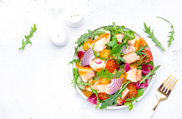 Fresh salad with grilled salmon and vegetables with arugula, radicchio, onion with lemon oil dressing. White background, top view