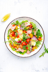 Tasty tuna vegetable salad with tomatoes, onion, corn, eggs, paprika, lettuce and arugula. White  background, top view