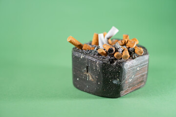Cigarette Butts in Ashtray on Green Background