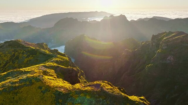 Aerial view at Pico do Arieiro of mountains over clouds with blooming Cytisus shrubs on sunset with sunburst. Madeira island, Portugal. Orbit parallax shot