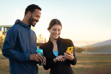 Multiracial couple checking fitness app on mobile phone after working out outdoors. Couple looking phone. Copy space.