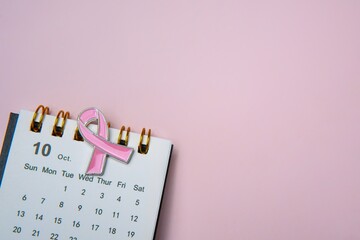 A calendar opened to the month of October and a pink ribbon, symbolizing breast cancer awareness. Copy space for text.