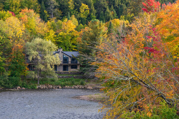 A tranquil river bank cabin surrounded by autumn forest. Colorful fall foliage landscape. Quebec, Canada.