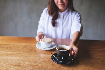 Closeup image of a young woman holding and serving two cups of hot coffee