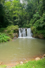 Amazing scenery of waterfall which water stream flowing from the cascade range into the pond surrounded by lush foliage vegetation in the tropical rainforest. Ton Yai Waterfall, Thailand.