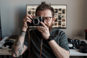 A focused photographer with tattoos using a vintage camera in a studio environment with photography equipment in the background.