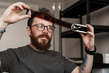 A man holding a film strip to the light, checking photographic negatives in a modern indoor setting.