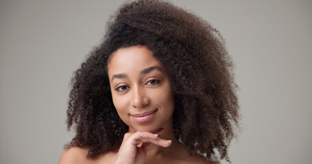 Beauty and healthcare concept - beautiful African American woman with curly afro hairstyle and clean, healthy skin touching face with hand, doing facial massage, posing and looking at camera