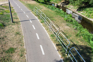 Bike trail through green park. Top view road background. Urban transportation landscape. Empty cycling path. Metal safety barriers. Bike line along river outdoor in nature. Sunny day in city park.