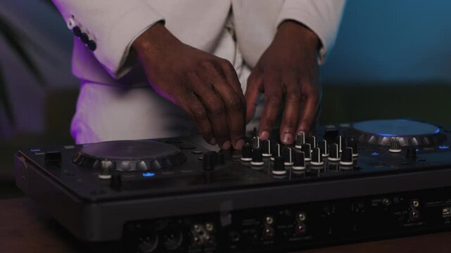 Close-up shot of a DJ in stylish white jacket skillfully working the turntables during a live performance. The DJ's hands are adjusting knobs and sliders on the mixer, creating the perfect sound mix.