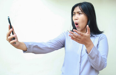 pretty asian young business woman shocked looking mobile phone hold on hands raising palm, questioning gesture, wearing formal shirt standing over isolated white background