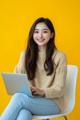 Naklejka premium Young Asian woman smiling happy. While she is using a laptop, sitting on a white chair and looking isolated on a yellow copy space background. 