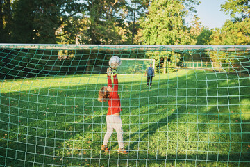 Little boy playing football with his father, kid goalkeeper defending the goal