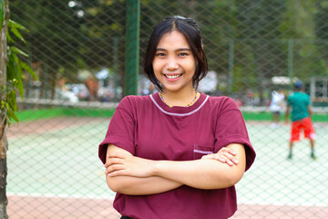 happy asian woman standing in tennis court with cross arms look at camera with confidence