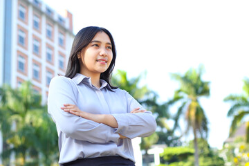 success asian businesswoman wear formal suit cross hand standing over urban building, agent insurance smiling confident looking away show optimistic expression