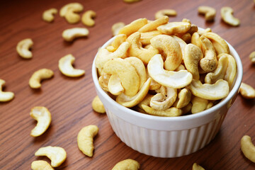 Bowl Full of Dried Cashew Nuts with Some Kernels Scattered on Wooden Table