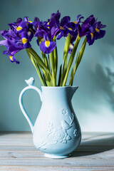 Close-up bouquet of purple flowers in blue ceramic jug on wooden table against the background of glare from the sun. Vertical. Close-up