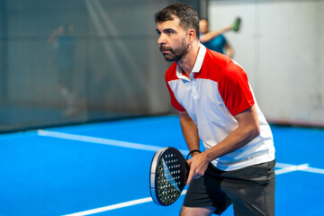 Mature sportive man playing paddle tennis indoors