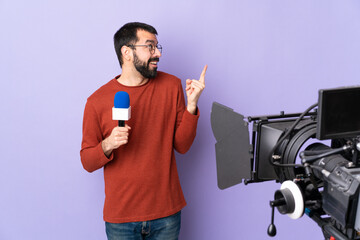 Reporter man holding a microphone and reporting news over isolated purple background intending to realizes the solution while lifting a finger up