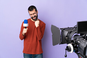 Reporter man holding a microphone and reporting news over isolated purple background celebrating a victory