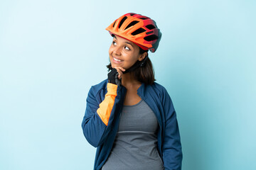 Young cyclist woman isolated on blue background looking up while smiling