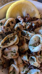 closeup of grilled calamaris garnished with parsley and served with a wedge of lemon. The seafood dish highlights the tender texture and fresh flavors of mediterranean cuisine