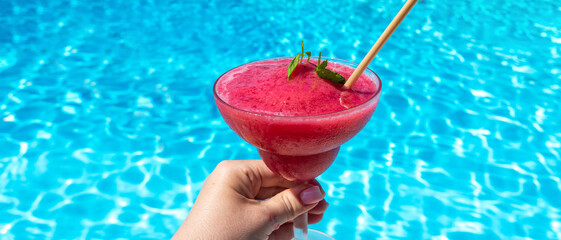 Chilled raspberry or strawberry Daiquiri with mint in hand by pool on sunny day. Concept of summer...