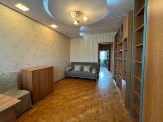 Bright room with parquet floors, bookshelves, sofa, and a desk by large windows. Ideal for a home office or study. Stylish design and plenty of natural light.