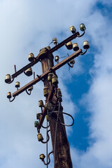 A rustic utility pole with aged ceramic insulators stands tall under a blue sky, highlighting the...