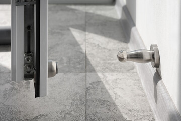 Close-up a stainless steel door stopper and metal-plastic door in a house.
