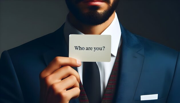 Close up of a man in a suit holding a card with Who Are You? printed on it, questioning identity and self perception