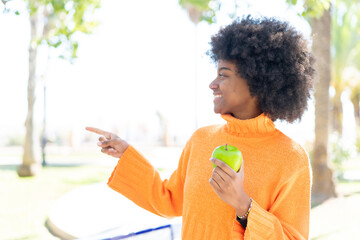 African American girl with an apple at outdoors pointing to the side to present a product