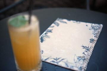 Restaurant or bar menu, placed on a table. The center of the menu is white and free for text.
A cocktail is blurred in the foreground.
