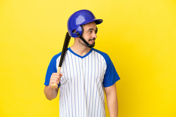 Young caucasian man playing baseball isolated on yellow background looking side