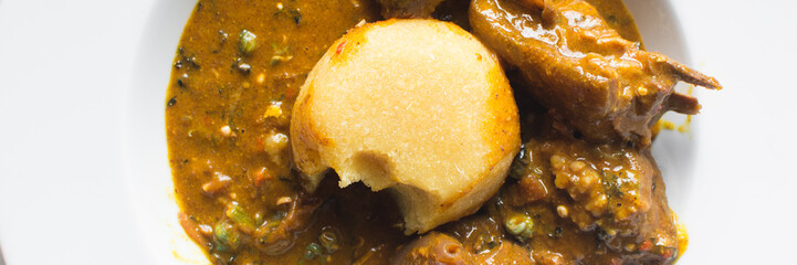 Overhead view of nigerian ogbono soup and eba on a white plate, top view of ogbono draw soup with garri and assorted meats in a soup plate