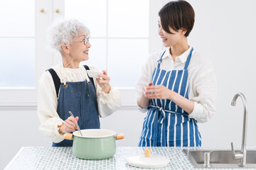 キッチンに立つ若い女性とシニア女性　料理イメージ