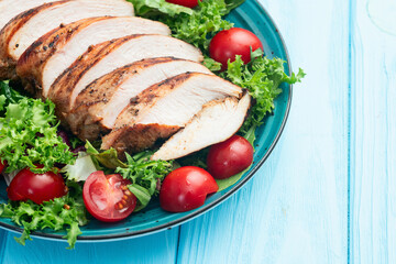 Grilled chicken breast ( fillet ) with lattuce salad and cherry tomatoes . Top view