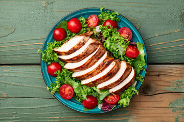 Grilled chicken breast ( fillet ) with lattuce salad and cherry tomatoes . Top view