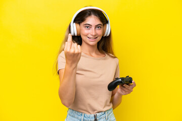 Young caucasian woman playing with a video game controller isolated on yellow background doing coming gesture