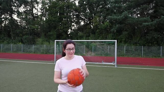 young girl holding and twirling a soccer ball in her hands and smiling broadly. woman on a large soccer field in the evening with soccer goals in the background. outdoor sports and training.