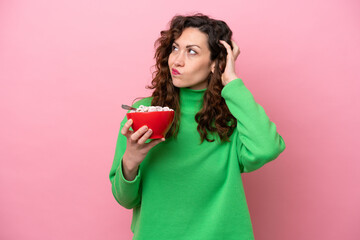 Young caucasian woman holding a bowl of cereals isolated on pink background having doubts and with confuse face expression