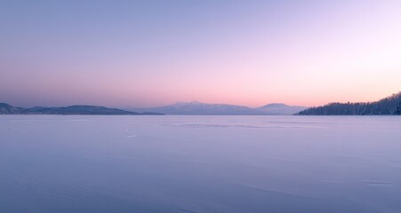 Obraz premium A serene winter morning unfolds over a frozen lake, with soft pastel hues illuminating the distant mountains and trees