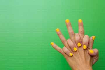 A woman's hands clasped tightly with her nails painted yellow on a green background.