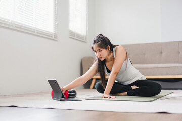 Obraz premium Young Asian woman at home doing exercise in front of open laptop, repeating instructions by professional online fitness trainer.