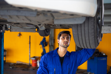 car lift under vehicle. Portrait hispanic latin male mechanic repairs car in garage. Car repair maintenance and auto service garage concept