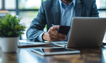 Middle-aged professional man using smartphone, laptop, tablet on desk - busy office work, business meeting preparation